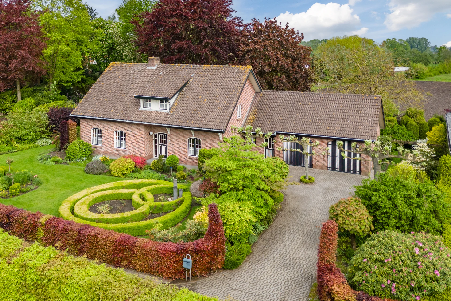 Dronefoto van een landelijke woning met bijgebouw en aangelegde tuin
